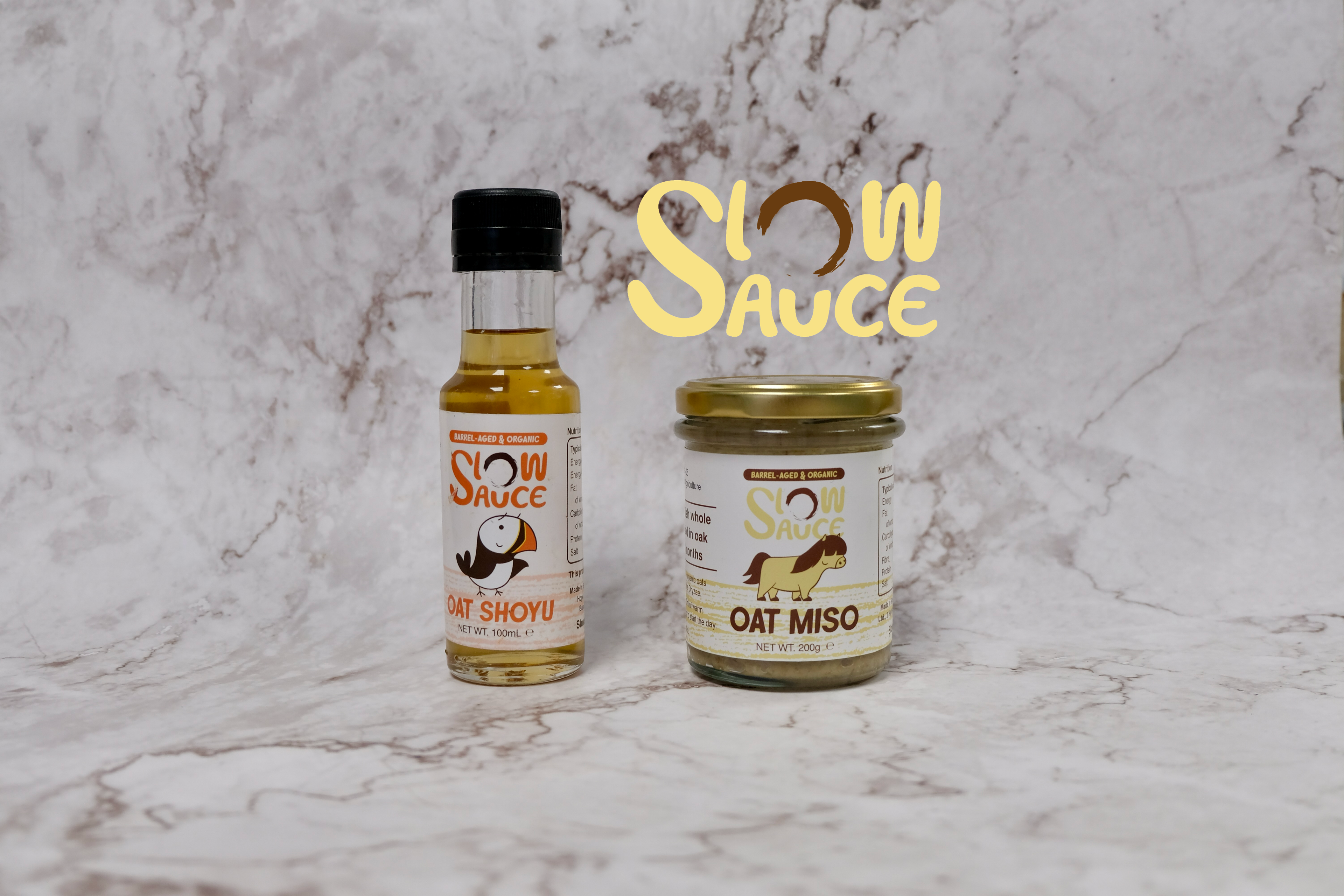 Slow Sauce organic barrel-aged oat shoyu and oat miso in retail packaging displayed on a marble background