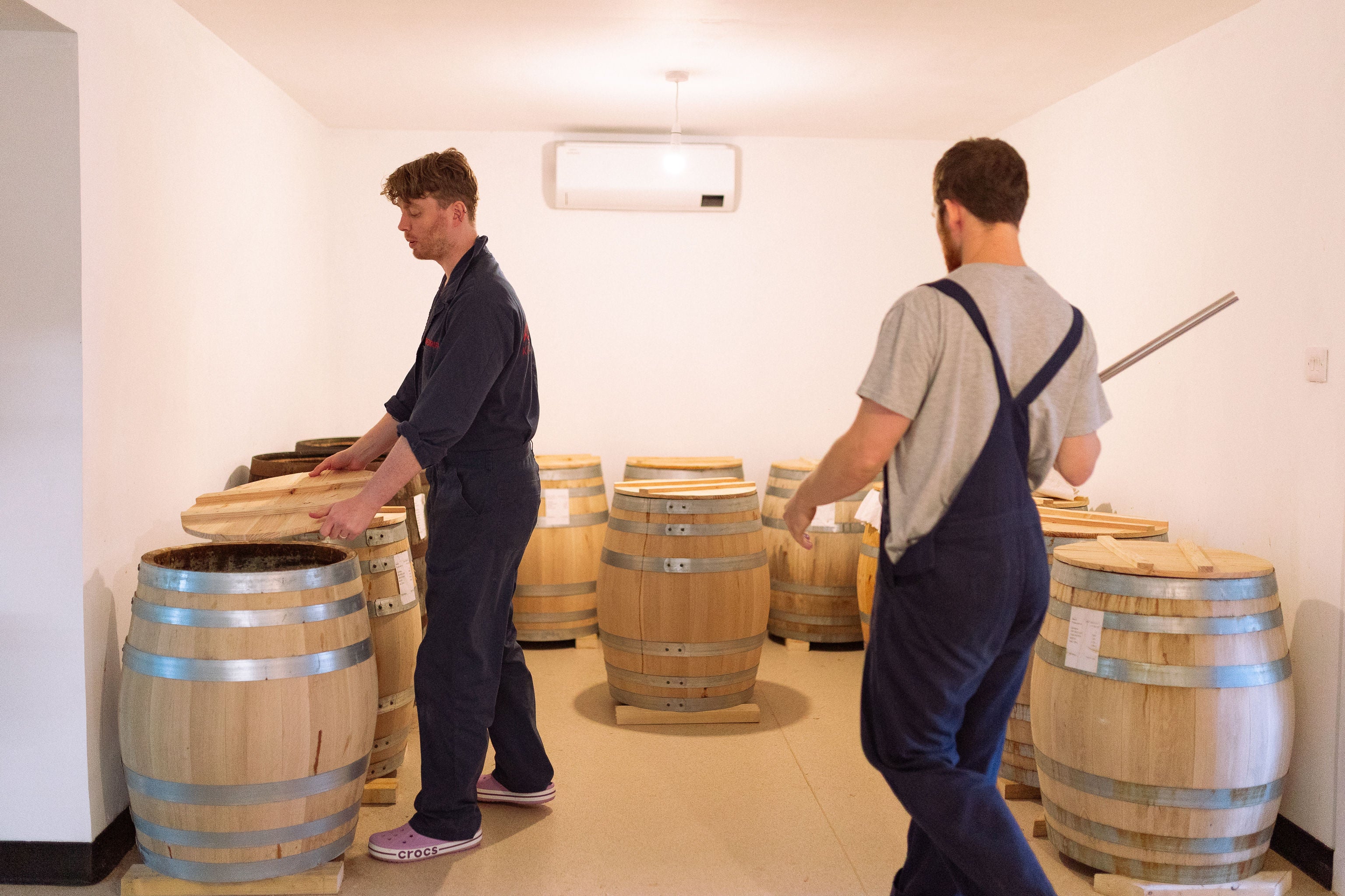 Two brewers moving between rows of oak fermentation barrels at Slow Sauce's Banchory brewery.